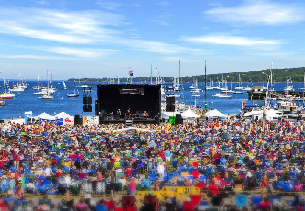 A large crowd at the harbor enjoying live music.